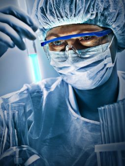 Portrait of scientist Vertical shot of woman in eyeglasses and uniform looking at a tube with tested sample